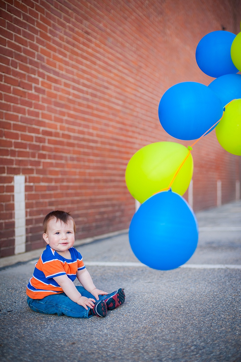 One year old with balloons next to brick wall
