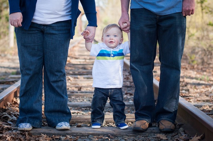 Parents holding their son's hands standing on train tracks