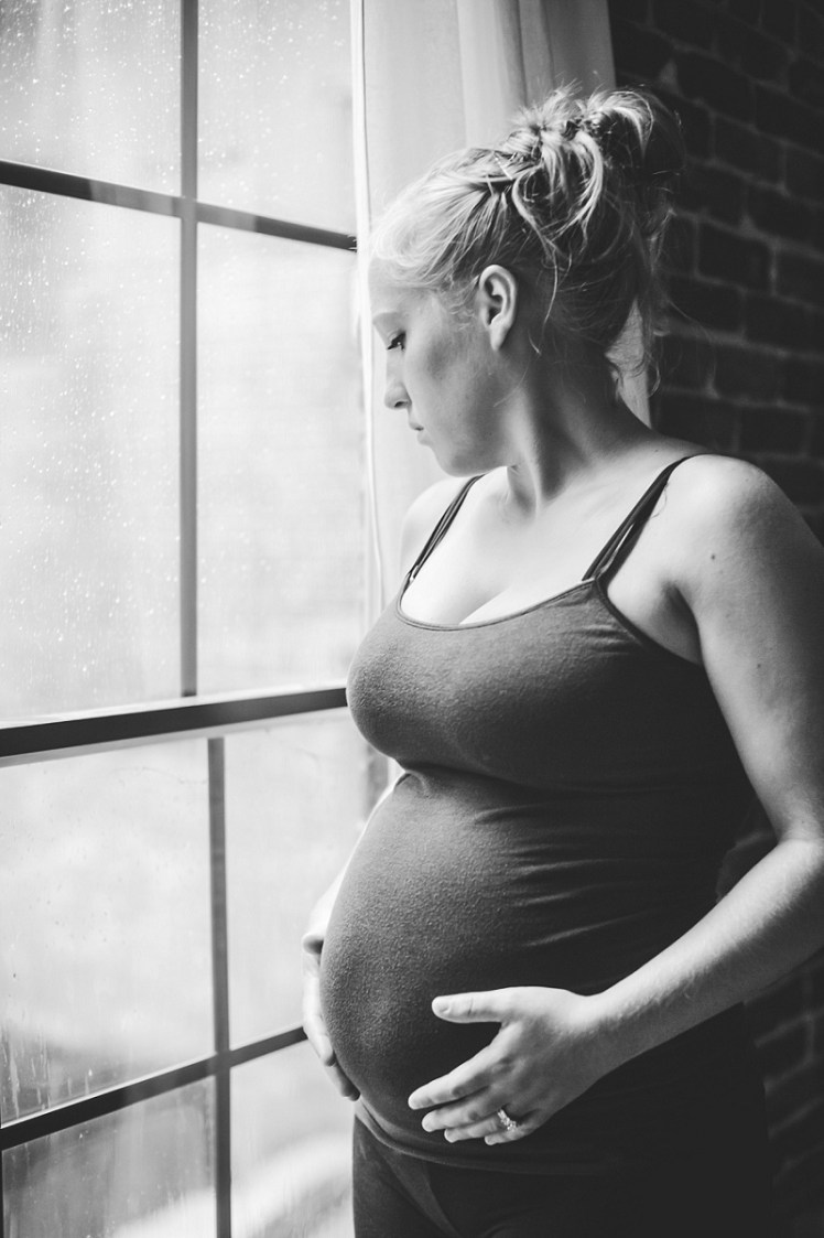 Pregnant woman standing next to window holding her belly