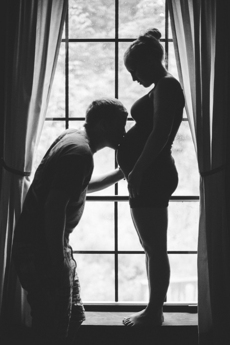 Black and white silhouette of pregnant woman and man kissing her belly