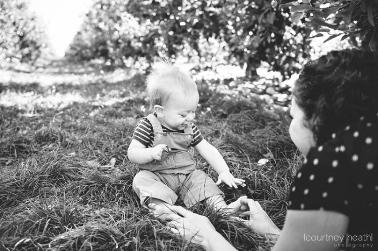 Black and white mother smiling at baby in apple orchard